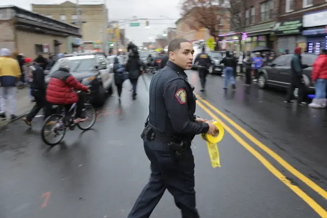 A police officer pushes pedestrians back from the scene of a shooting in Jersey City, N.J.