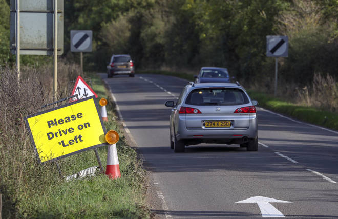 A vehicle with diplomatic plates passes a Please Drive on Left sign and road marking that have been placed on the B4031 outside RAF Croughton, in Northamptonshire, where Harry Dunn, 19, died.