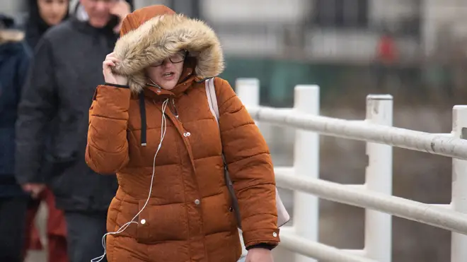 A woman shields herself from biting wind in London as temperatures are set to plummet