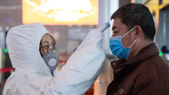 A Chinese medical worker wearing protective clothing checks body temperatures of passengers for prevention of the new coronavirus at the Nanjing South Railway Station
