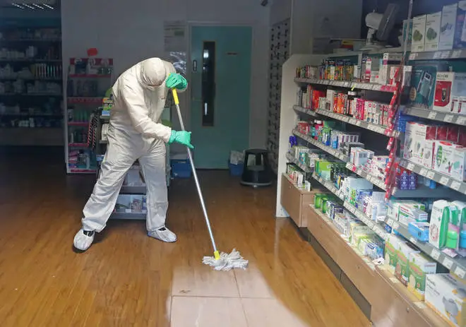 A cleaner in a hazmat suit disinfects a pharmacy in Brighton