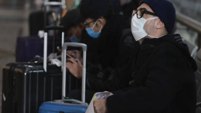 People wearing sanitary masks sit as they wait at the Centrale main railway station in Milan