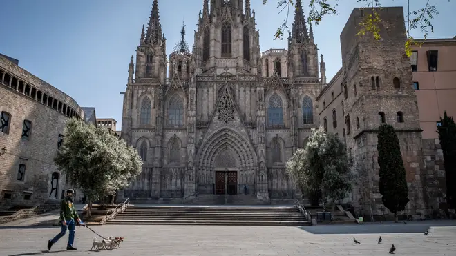 A man walking dogs past a deserted Cathedral of Barcelona during the period of confinement