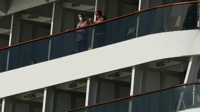 Passengers, one wearing a protective face mask, look out from the Zaandam cruise ship