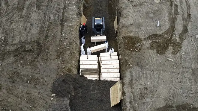 Workers wearing personal protective equipment bury bodies in a trench on Hart Island