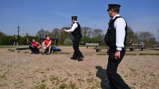 Police officers talk with a couple resting on Primrose Hill in London