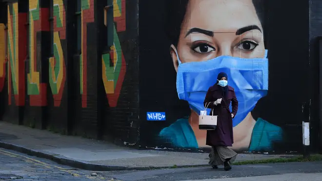 A woman wearing a face mask walks past a piece of street art depicting an NHS worker
