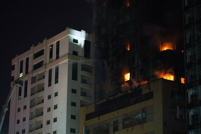 Firefighters battle a blaze burning on the side of a high-rise building in Sharjah, United Arab Emirates