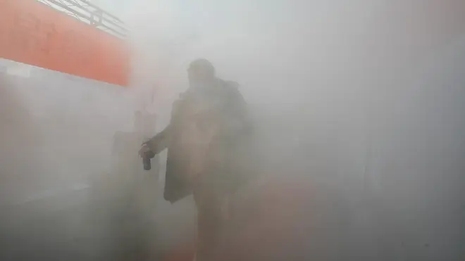 A resident walks through a temporary room of disinfectant spray to return home in north China