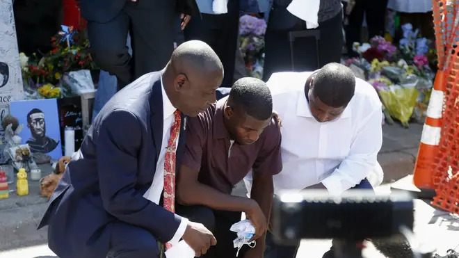 Mr Floyd's son Quincy Mason (centre) kneels with his uncle Twain Mason (right) and family lawyer Ben Crump (left) at a memorial site