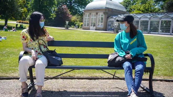 Two friends wearing face masks sit on a bench as they maintain social distancing at the Botanical Gardens , Sheffield