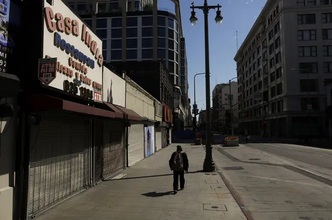 A man walks on a sidewalk lined with shuttered shops in Los Angeles
