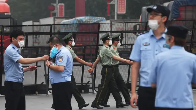 Paramilitary police officers march as police stand guard at the entrance to the closed Xinfadi market in Beijing