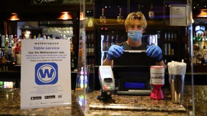 A member of staff in PPE waits to serve drinkers at the reopening The Toll Gate, a Wetherspoons pub in Hornsey, north London