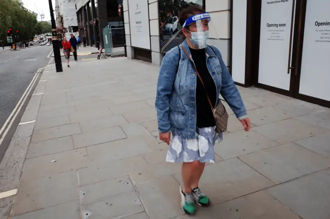 A woman wearing a face mask and face shield walks along Piccadilly in London