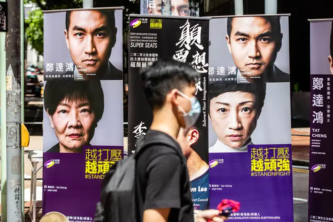 A man wearing a face masks walks past posters of pan-democratic candidates