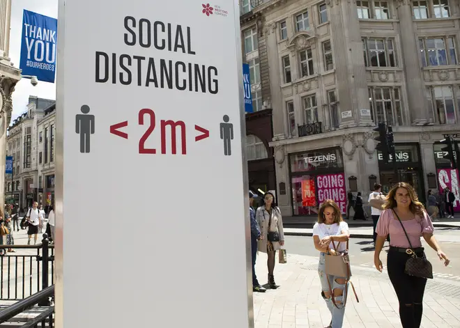 Shoppers walk past a social distancing sign in London