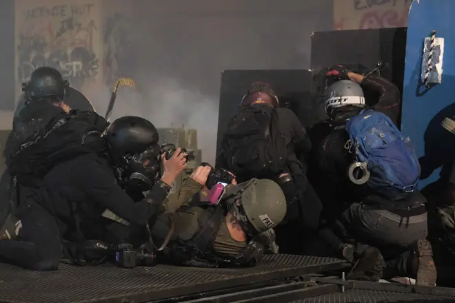 Press photographers take cover as officers fire tear gas at protesters