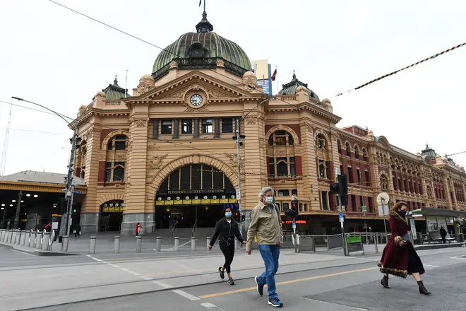 People wearing face masks cross the road outside Flinder Street Station in Melbourne