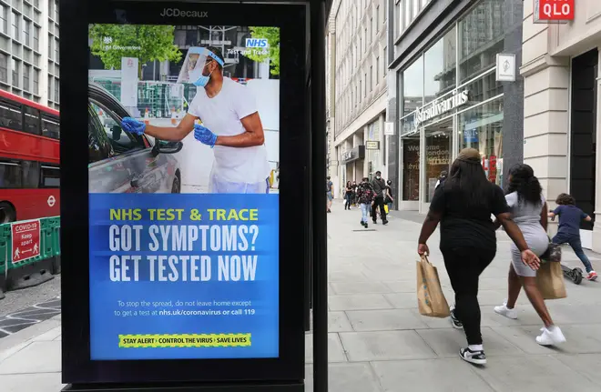 Shoppers walk past a screen on a bus stop displaying a NHS notice on test and trace on Oxford Street, London