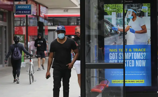 A pedestrian walks past a screen on a bus stop displaying a NHS notice on test and trace on Oxford Street
