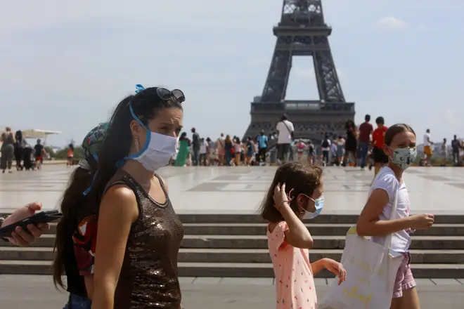 Tourists wearing protective masks walk in front of the Eiffel Tower