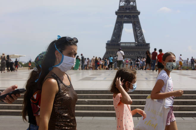 Tourists wearing protective masks walk in front of the Eiffel Tower