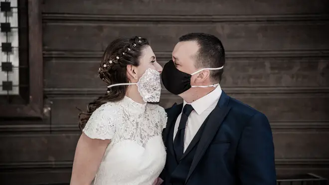 Newlyweds Silvia and Petar are seen kissing with protective masks in front Varna Wedding Ritual Home. Wedding during covid-19