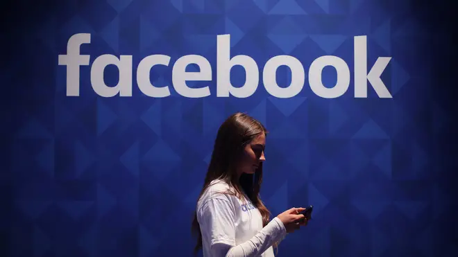 A woman looks at her smartphone in front of a Facebook logo