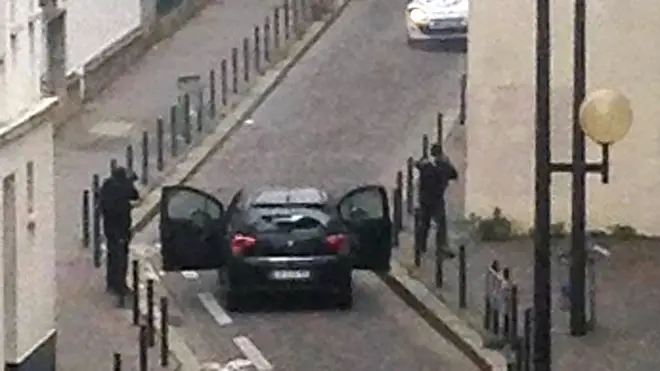Armed gunmen face police officers near the offices of the French satirical newspaper Charlie Hebdo in Paris on January 7, 2015