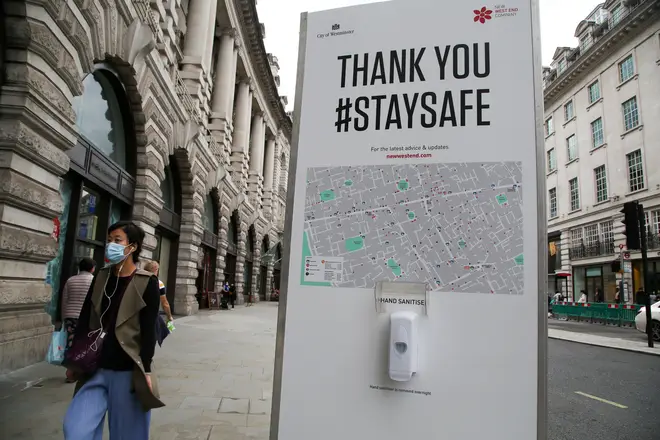 File photo: A woman wearing a face mask walks past a hand sanitizer station on Regents Street