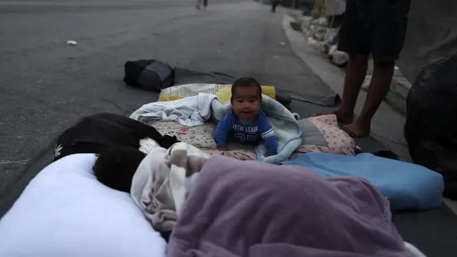 A baby crawls as migrants remain camped out on a roa