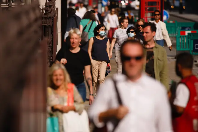 People, some wearing face masks, walk along Piccadilly in London