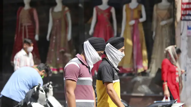 Indians wearing face masks as a precaution walk in a market area in Jammu