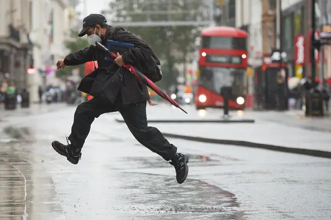 A man jumps over a puddle in London as Storm Alex brings heavy rain to the UK