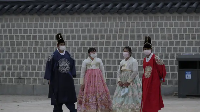 Visitors dressed in South Korean traditional “Hanbok” attire, wearing face masks as a precaution against the coronavirus, stand at the Gyeongbok Palace, one of South Korea’s well-known landmarks, in Seoul, South Korea (Lee Jin-man/AP)