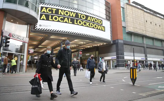 People wearing face masks walk past a advertisement on Market Street in Manchester