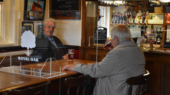 Regulars enjoy a drink at a table divided by a Perspex screen at the Royal Oak in Barton-under-Needwood, Staffordshire