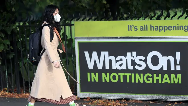 A woman in a mask walks past a sign reading: 'What's On! In Nottingham'