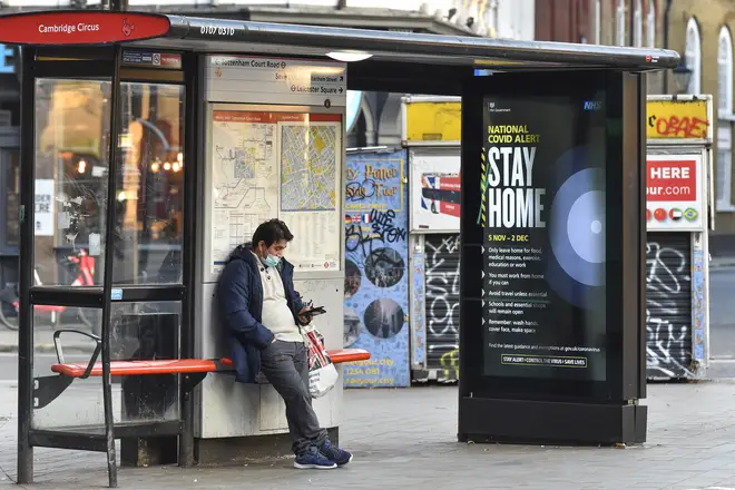 A man using his phone at a bus stop in Cambridge Circus, London