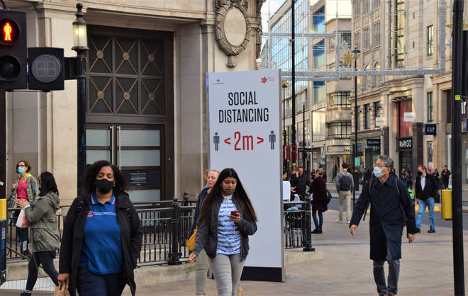 File photo: People wearing face masks as a precaution walking past a social distancing sign on Oxford Street
