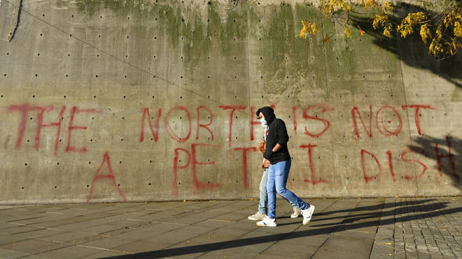 A couple walk past a sign saying "The north is not a petri dish"