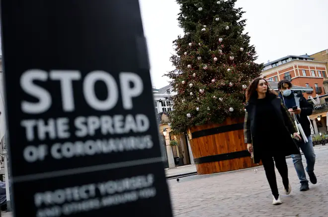 Pedestrians pass a COVID-19 sign reading "Stop the spread" as they walk past a Christmas tree in Covent Garden