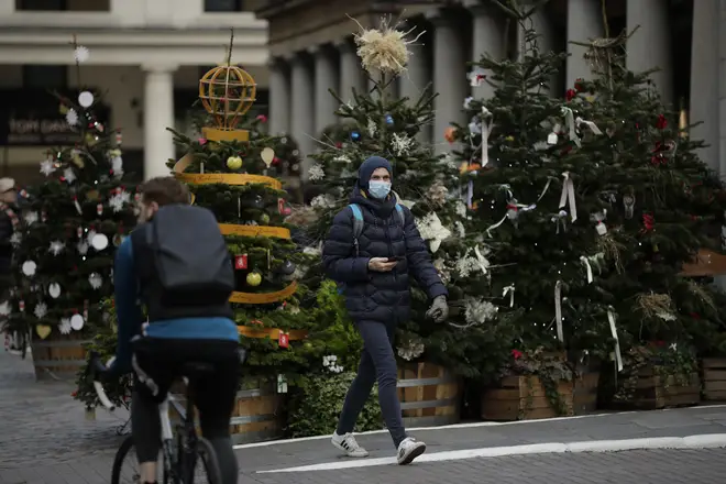 A man wearing a face mask walks past Christmas trees in Covent Garden