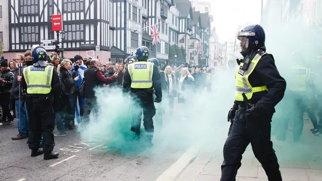 Green smoke rises from a flare thrown as anti-lockdown activists confront police officers