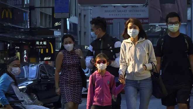 People wearing face masks to protect against coronavirus walk along a street in Hong Kong (KIn Cheung/AP)