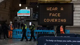 Police officers walk past a 'Wear a face covering' message displayed outside Victoria Station