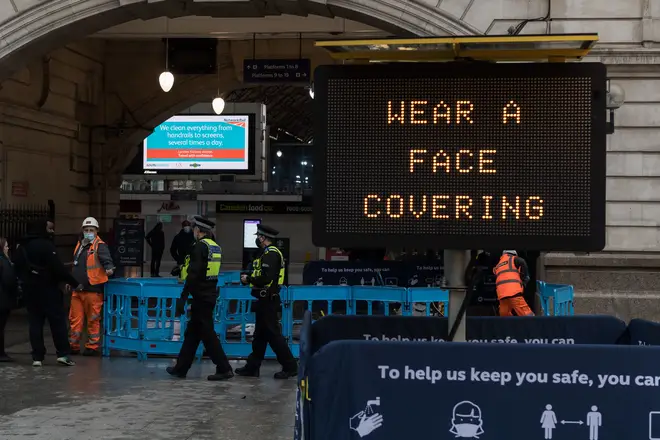 Police officers walk past a 'Wear a face covering' message displayed outside Victoria Station
