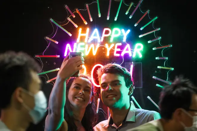 People seen having their photo taken in front of a neon Happy New Year sign as people wearing masks walk past during New Year's Eve celebrations on December 31, 2020 in Melbourne, Australia