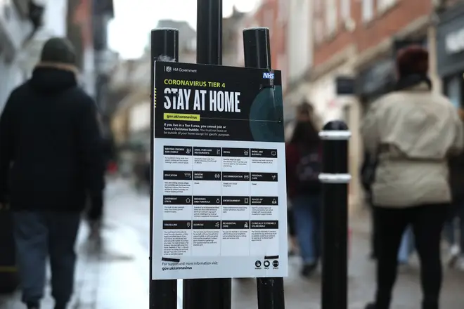 People make their way past a Government coronavirus Tier 4 sign saying 'Stay at Home' on the High street in Winchester